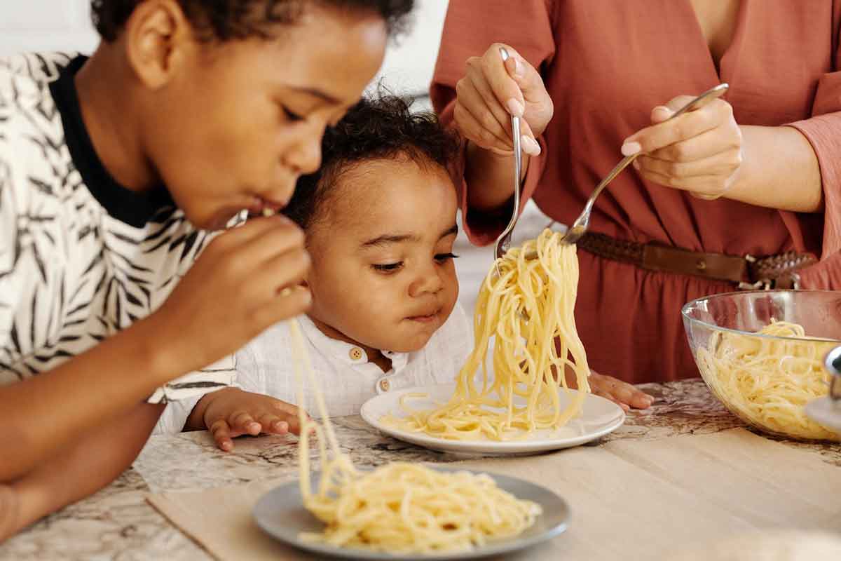 due bambini mangiano un piatto di spaghetti