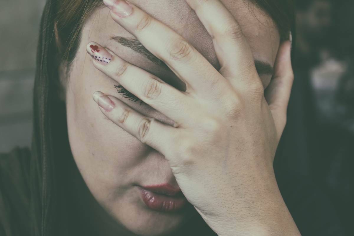 Donna dolorante si copre la faccia con la mano, soffre di endometriosi