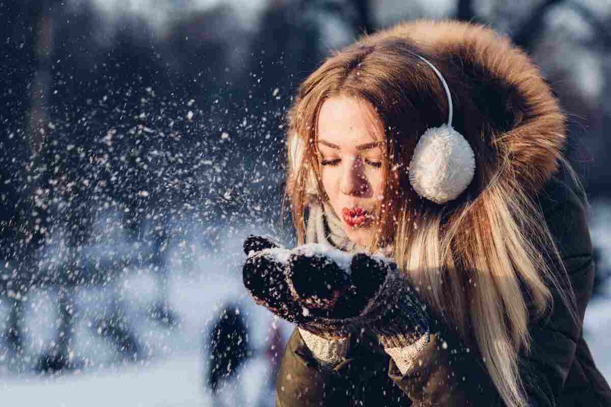 ragazza che soffia sulla neve vestita in modo pesante